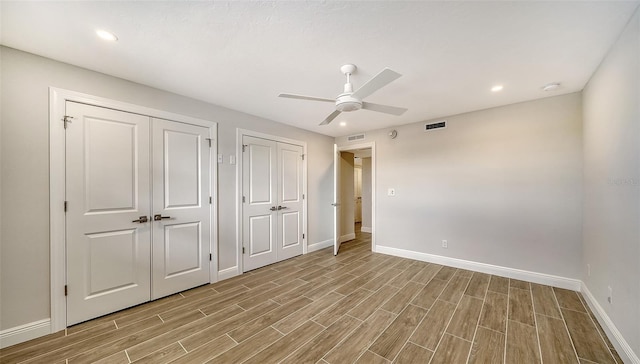 unfurnished bedroom with light wood-type flooring, ceiling fan, and multiple closets