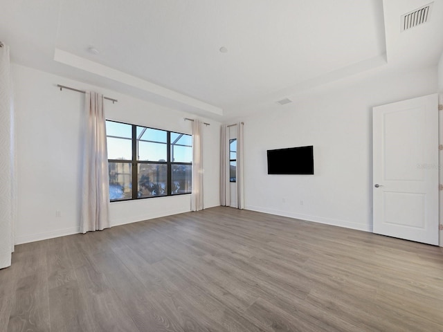 unfurnished living room featuring a tray ceiling, wood finished floors, visible vents, and baseboards