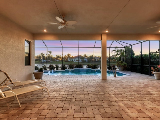 outdoor pool with glass enclosure, a water view, ceiling fan, a patio area, and a hot tub
