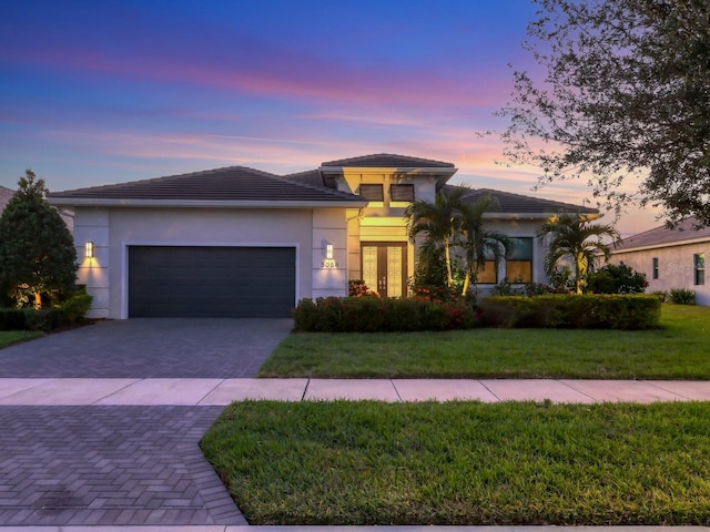 prairie-style house with a tile roof, decorative driveway, an attached garage, a front yard, and stucco siding