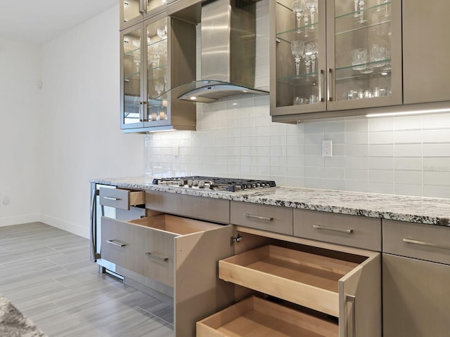 kitchen featuring wall chimney exhaust hood, baseboards, backsplash, and gray cabinets