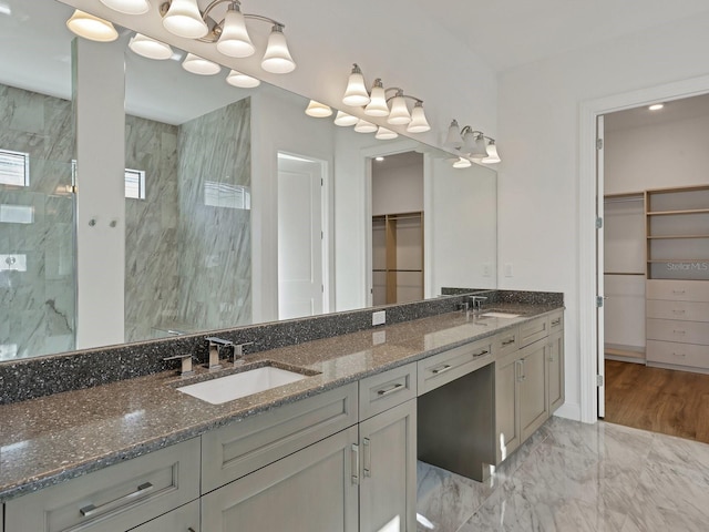 full bath featuring a spacious closet, a marble finish shower, and a sink
