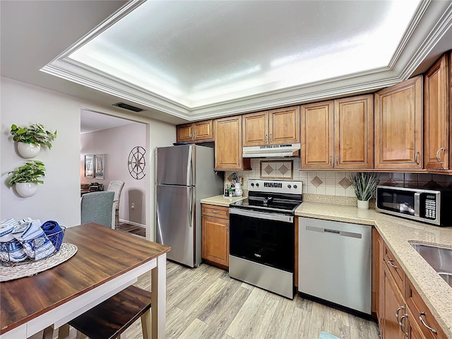 kitchen with stainless steel appliances, a raised ceiling, crown molding, light hardwood / wood-style floors, and decorative backsplash