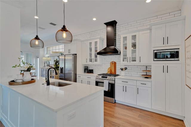 kitchen featuring appliances with stainless steel finishes, wall chimney exhaust hood, sink, white cabinets, and hanging light fixtures