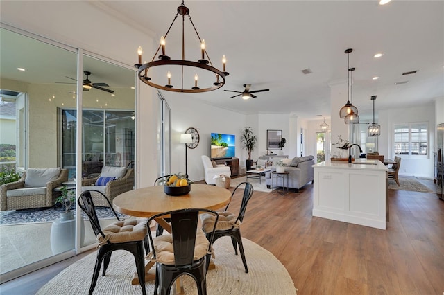 dining area with crown molding, sink, ceiling fan with notable chandelier, and hardwood / wood-style flooring