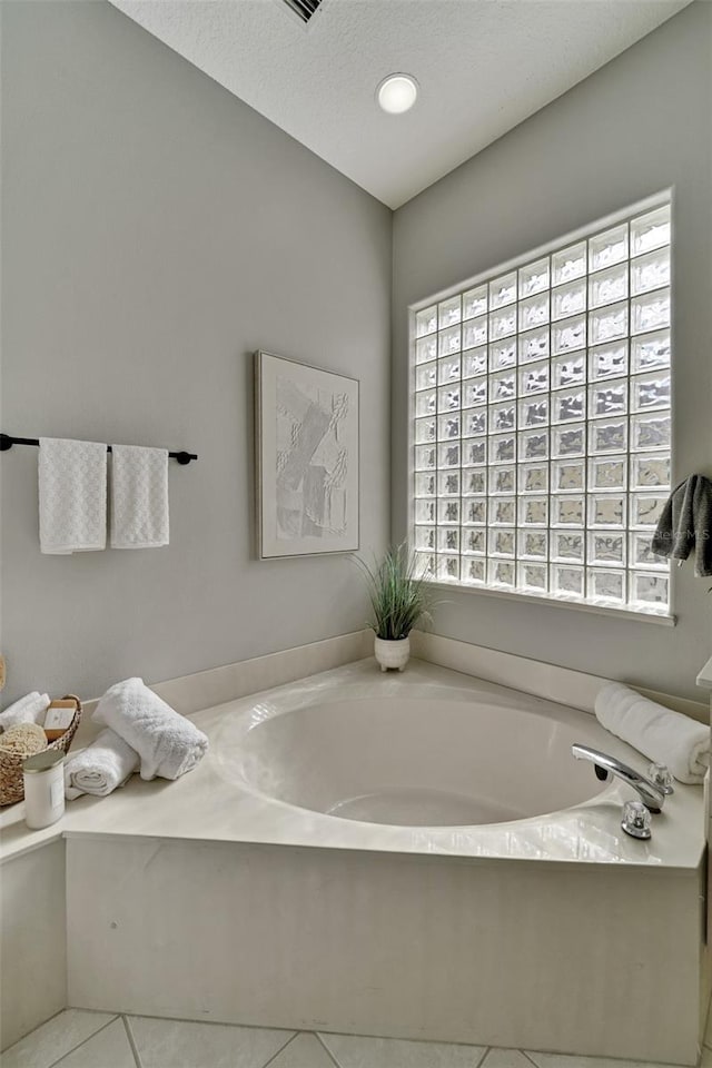 bathroom with tile patterned floors, a bathtub, a healthy amount of sunlight, and a textured ceiling