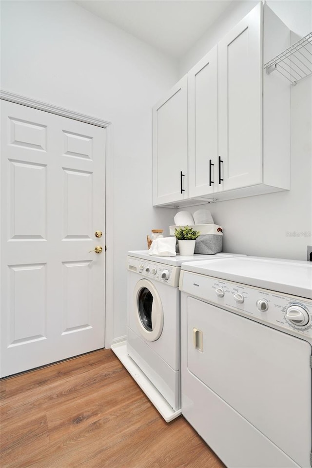 laundry area with washer and dryer, light wood-type flooring, and cabinets