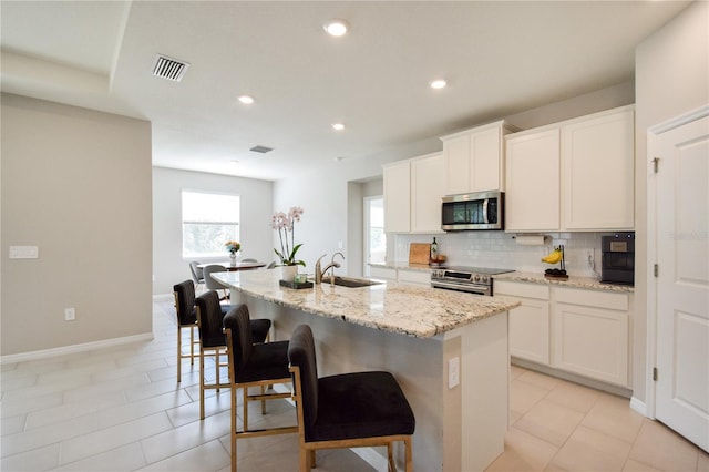 16926 Harvest Moon Way, Bradenton, FL 34211 - kitchen with stainless steel appliances, a sink, a kitchen island with sink, decorative backsplash, and light stone countertops