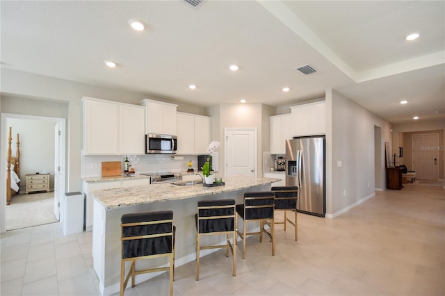 16926 Harvest Moon Way, Bradenton, FL 34211 - kitchen with stainless steel appliances, backsplash, a center island with sink, a kitchen bar, and white cabinets