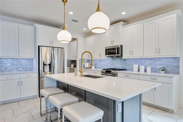 kitchen with decorative backsplash, appliances with stainless steel finishes, a kitchen island with sink, white cabinetry, and hanging light fixtures