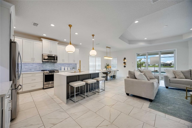 kitchen with tasteful backsplash, stainless steel appliances, a kitchen island with sink, decorative light fixtures, and white cabinetry