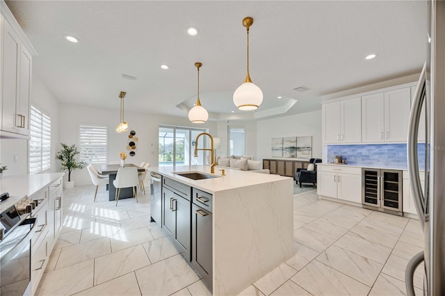 kitchen featuring hanging light fixtures, backsplash, a kitchen island with sink, white cabinets, and appliances with stainless steel finishes