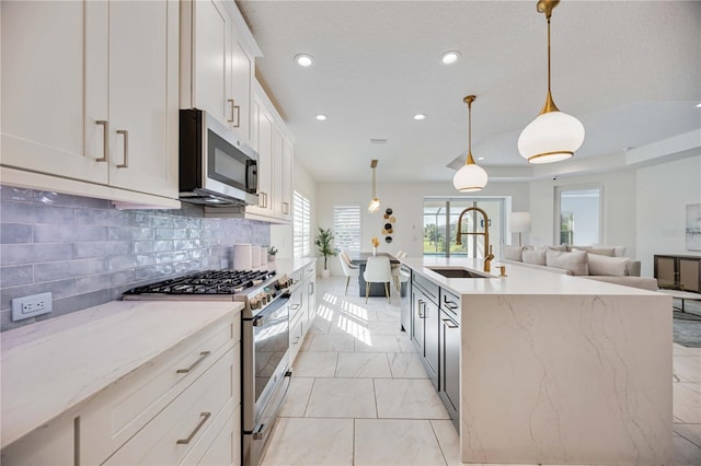 kitchen featuring sink, hanging light fixtures, an island with sink, white cabinets, and appliances with stainless steel finishes