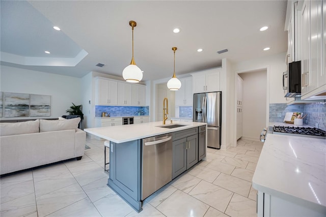 kitchen with hanging light fixtures, backsplash, an island with sink, white cabinets, and appliances with stainless steel finishes