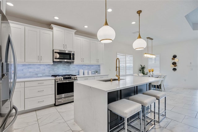 kitchen with pendant lighting, stainless steel appliances, white cabinetry, and a center island with sink