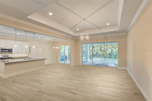 unfurnished living room with a raised ceiling, an inviting chandelier, ornamental molding, and light wood-type flooring