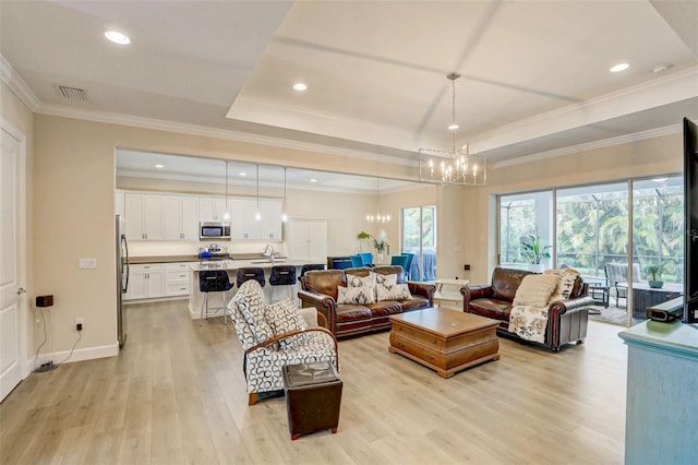 living room with sink, a raised ceiling, a notable chandelier, light hardwood / wood-style floors, and ornamental molding