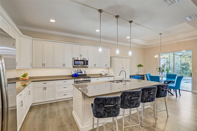 kitchen featuring sink, pendant lighting, a kitchen island with sink, white cabinets, and appliances with stainless steel finishes