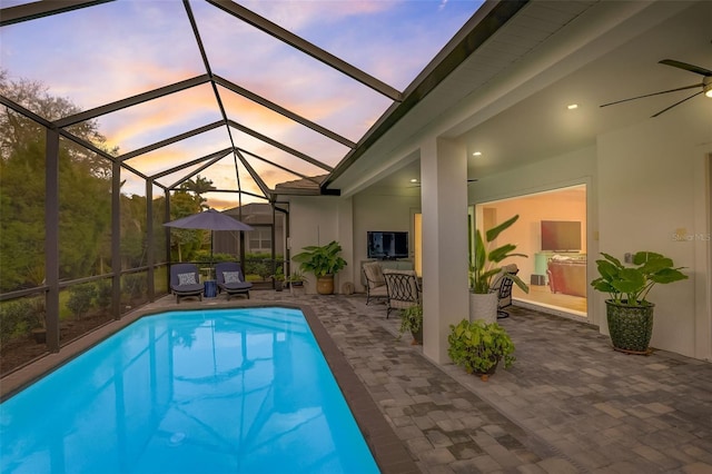 pool at dusk with glass enclosure, ceiling fan, and a patio area