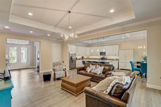 living room featuring a raised ceiling, light hardwood / wood-style flooring, ornamental molding, and an inviting chandelier