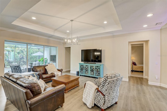 living room featuring a raised ceiling, light hardwood / wood-style flooring, ornamental molding, and a notable chandelier