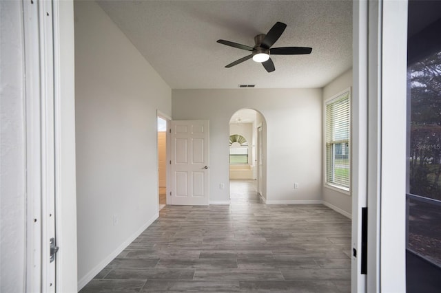 empty room with arched walkways, a textured ceiling, visible vents, baseboards, and dark wood-style floors