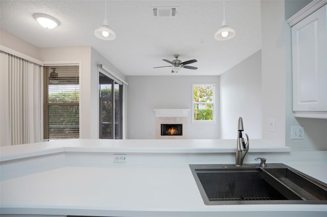 kitchen with a warm lit fireplace, hanging light fixtures, a sink, and visible vents