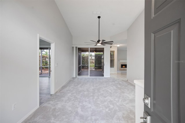 unfurnished living room with a ceiling fan, light carpet, high vaulted ceiling, a lit fireplace, and baseboards