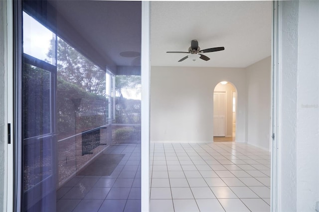 tiled empty room with arched walkways, ceiling fan, and baseboards