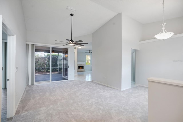 carpeted spare room featuring a warm lit fireplace, high vaulted ceiling, a ceiling fan, visible vents, and baseboards