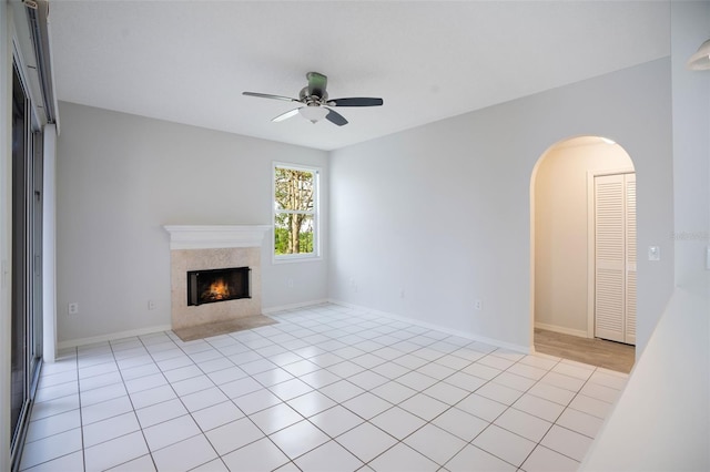 unfurnished living room featuring arched walkways, a ceiling fan, a high end fireplace, light tile patterned flooring, and baseboards