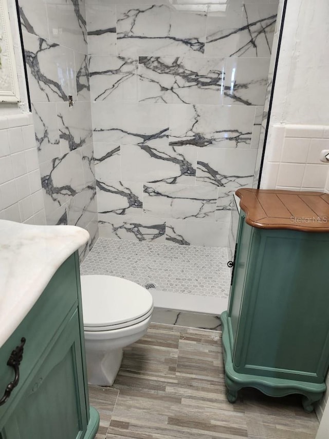 bathroom featuring vanity, toilet, tiled shower, and tile walls