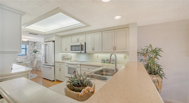 kitchen with white appliances, a raised ceiling, sink, light wood-type flooring, and a textured ceiling