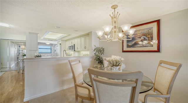 dining area featuring sink, light hardwood / wood-style floors, a textured ceiling, and an inviting chandelier