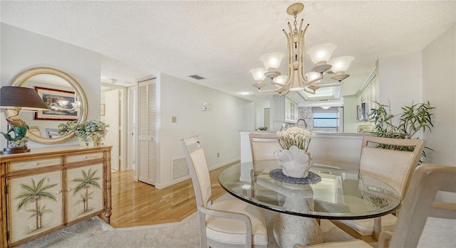 dining area with light wood-type flooring, a textured ceiling, and an inviting chandelier