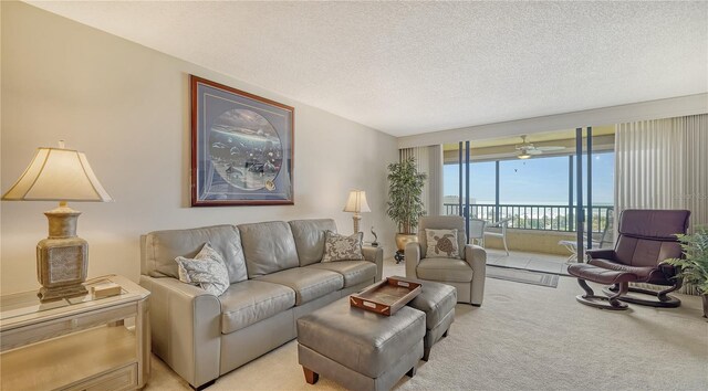 carpeted living room with ceiling fan, a wall of windows, and a textured ceiling