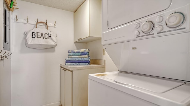 clothes washing area with a textured ceiling, electric panel, and stacked washer and clothes dryer