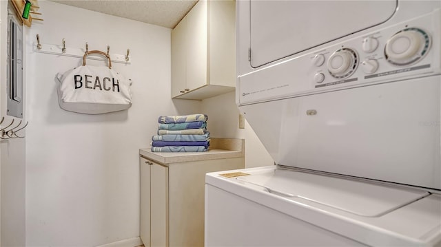 clothes washing area featuring laundry area, a textured ceiling, baseboards, and stacked washer / dryer