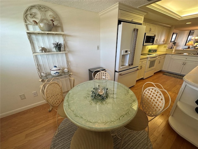 kitchen with wood finished floors, white appliances, baseboards, light countertops, and a sink