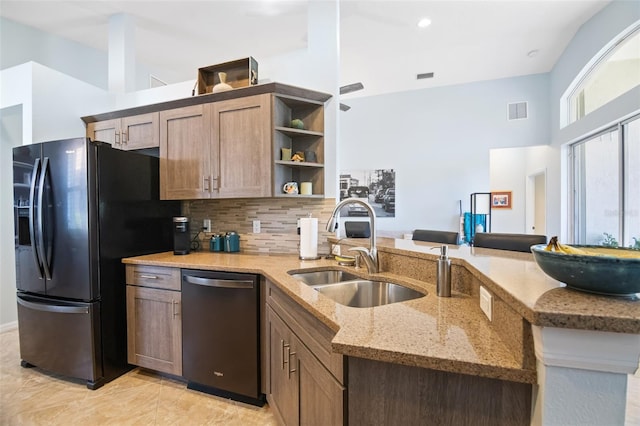 kitchen with kitchen peninsula, black fridge, light stone counters, stainless steel dishwasher, and sink