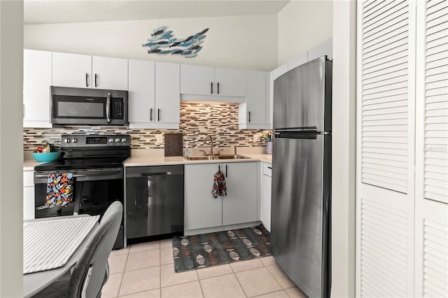 kitchen featuring white cabinetry, sink, lofted ceiling, light tile patterned floors, and appliances with stainless steel finishes