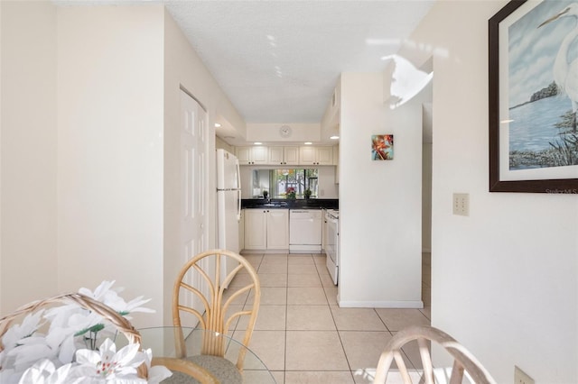 kitchen featuring a textured ceiling, sink, light tile patterned floors, and white appliances