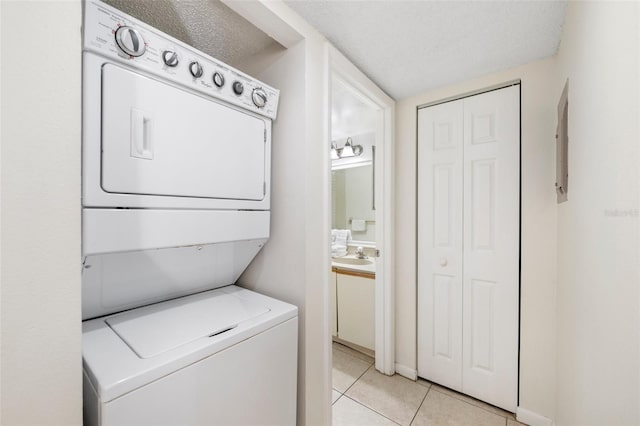 washroom featuring stacked washer and dryer, light tile patterned floors, a textured ceiling, and sink