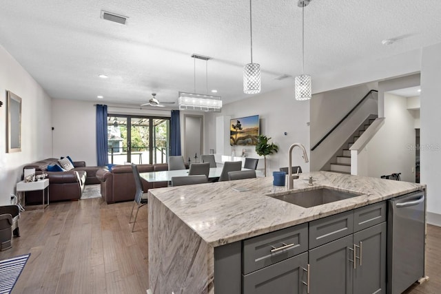 kitchen featuring light stone counters, dark wood-type flooring, sink, pendant lighting, and an island with sink