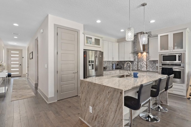 kitchen with a center island with sink, wall chimney range hood, sink, a textured ceiling, and appliances with stainless steel finishes