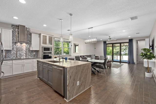 kitchen featuring appliances with stainless steel finishes, wall chimney exhaust hood, sink, dark hardwood / wood-style floors, and hanging light fixtures