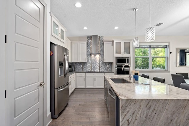 kitchen with white cabinetry, sink, hanging light fixtures, wall chimney range hood, and appliances with stainless steel finishes