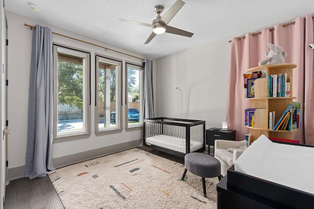 bedroom with a textured ceiling, ceiling fan, a crib, and hardwood / wood-style flooring