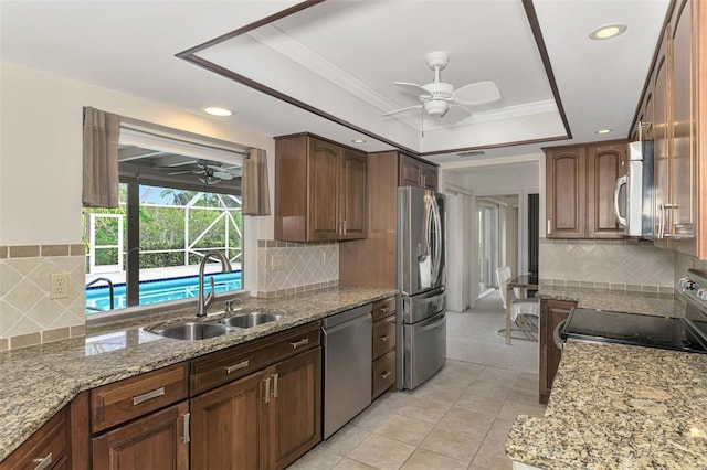 kitchen with ceiling fan, sink, a raised ceiling, light stone counters, and appliances with stainless steel finishes