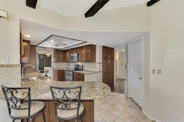 kitchen featuring kitchen peninsula, light stone counters, sink, and appliances with stainless steel finishes